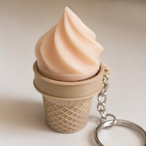 May include: A keychain featuring a light beige ice cream cone with a swirled, pale pink soft-serve top. The cone has a textured waffle pattern and is attached to a silver-toned metal chain and a circular split ring for keys.