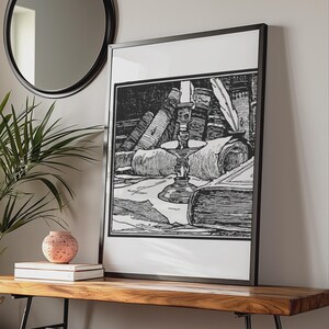 May include: A black and white framed print featuring a detailed line art illustration of a candle in a holder, a quill pen, a rolled parchment scroll, and several stacked books. The artwork is presented in a thin black frame with a white mat border.
