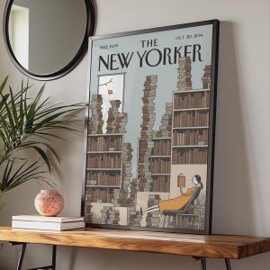 Könnte beinhalten: Ein gerahmter Druck des The New Yorker Magazin-Covers vom 20. Oktober 2014. Die Illustration zeigt eine Person in einem orangefarbenen Kleid, die in einem Sessel ein Buch liest, umgeben von hohen, wackeligen Stapeln brauner Bücher vor hellblauem Hintergrund.