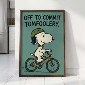 May include: A framed print showing Snoopy on a bicycle, wearing a helmet and collar. The text reads "OFF TO COMMIT TOMFOOLERY." The background is teal, and the frame is brown. A fun, cartoon-style image.