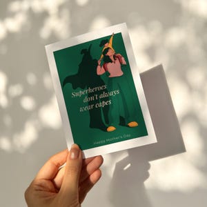 Könnte beinhalten: Eine Grußkarte mit grünem Hintergrund und dem Text "Superhelden tragen nicht immer Umhänge." Die Illustration zeigt eine Mutter, die ein Kind auf ihren Schultern trägt. Auf der Karte steht auch "Happy Mother's Day."
