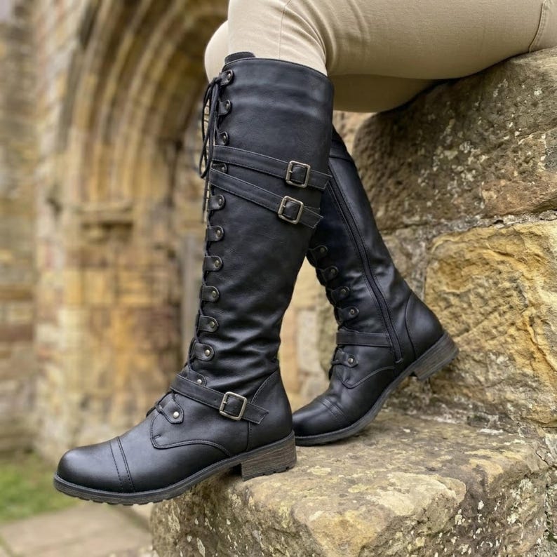 May include: A pair of black knee-high boots featuring a lace-up front design with metal eyelets, two horizontal buckled straps across the upper shaft, and a single buckled strap across the lower foot area, finished with a low block heel.