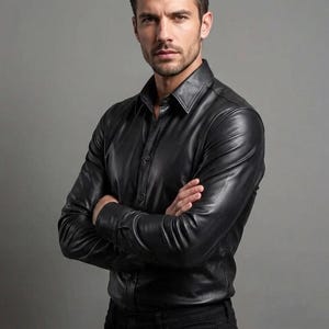 May include: A black leather button-down shirt with a classic collar. The long-sleeved shirt has a tailored fit and is buttoned up. The model in the image has their arms crossed.