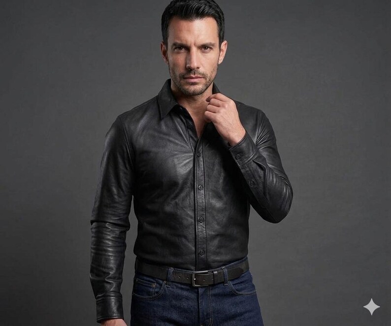 May include: A black leather shirt with long sleeves and a button-down front. The shirt is paired with blue jeans and a black belt. The model is wearing the shirt and looking at the camera.