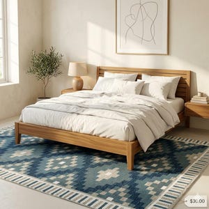 May include: A wooden bed frame with a headboard, dressed with white bedding, sits on a blue patterned rug. A small potted plant and a lamp are on a wooden nightstand. A framed abstract art piece hangs on the wall.
