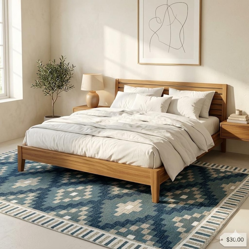 May include: A wooden bed frame with a headboard, dressed with white bedding, sits on a blue patterned rug. A small potted plant and a lamp are on a wooden nightstand. A framed abstract art piece hangs on the wall.