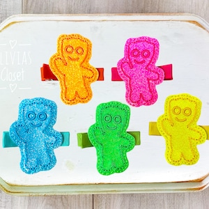May include: Five colorful gummy bear hair clips with a white background. The gummy bears are yellow, pink, blue, green, and orange. The text "Olivias Closet" is visible in the background.