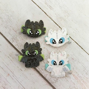 May include: Four handmade hair clips featuring dragon designs. Two clips are black with green accents, and two are white with blue accents. Each clip has a small ribbon and is labeled "Left" or "Right".
