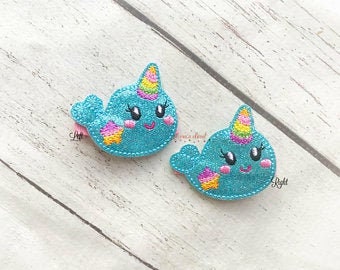 May include: Two turquoise glitter hair clips with a narwhal design. Each narwhal has a rainbow horn, pink cheeks, and a star on its tail.