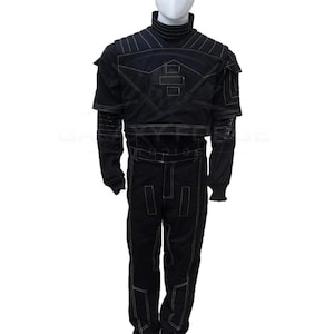 May include: Black costume with white stitching, featuring a high collar and long sleeves. The outfit includes a jacket with shoulder accents and matching pants. The design incorporates geometric shapes and lines, creating a futuristic aesthetic. The costume is displayed on a mannequin.
