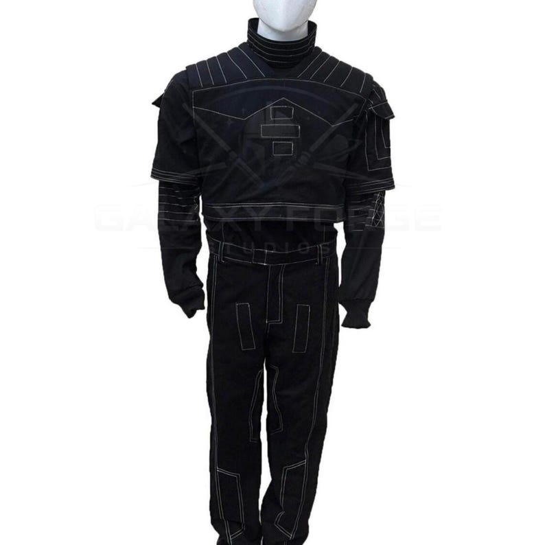 May include: Black costume with white stitching, featuring a high collar and long sleeves. The outfit includes a jacket with shoulder accents and matching pants. The design incorporates geometric shapes and lines, creating a futuristic aesthetic. The costume is displayed on a mannequin.