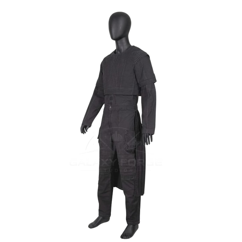 Op de afbeelding: Een zwarte jumpsuit op een etalagepop, voorzien van een gestructureerd lijfje met verticale stiksels, lange mouwen en een gelaagd rokpaneel. Het kledingstuk heeft meerdere zakken op de broekspijpen en een ronde halslijn in een effen zwarte kleur.