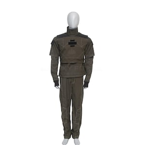 May include: A dark olive green tactical uniform set consisting of a long-sleeved top with a high collar, structured shoulder panels, and a black rectangular patch on the chest, paired with matching trousers featuring visible light-colored stitching.