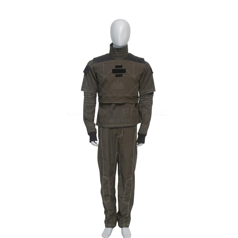 May include: A dark olive green tactical uniform set consisting of a long-sleeved top with a high collar, structured shoulder panels, and a black rectangular patch on the chest, paired with matching trousers featuring visible light-colored stitching.