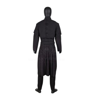 Op de afbeelding: Een zwarte set bestaande uit een tuniek met lange mouwen en een broek op een etalagepop. De tuniek heeft een hoge kraag, een gestructureerde schouderbedekking en een geplooid rokgedeelte dat tot op de knie&euml;n valt. Het kledingstuk is zwart met zichtbare stiksels.