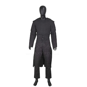 Op de afbeelding: Een zwart kostuumset op een etalagepop, bestaande uit een gestructureerd borststuk met verticale stiksels, lange mouwen en een bijpassende broek met verstevigde kniestukken en een lange, aan de voorzijde open overjas.