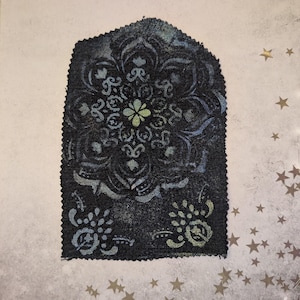May include: A dark blue fabric patch with a detailed floral mandala design. The design features a central flower and surrounding patterns in shades of blue and green. The patch has a decorative, arched top and a raw edge.