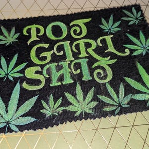 May include: Black rectangular doormat with the words "Poo Girl Shit" in green, surrounded by green cannabis leaves. The text and leaves have a gradient effect, with lighter green highlights.