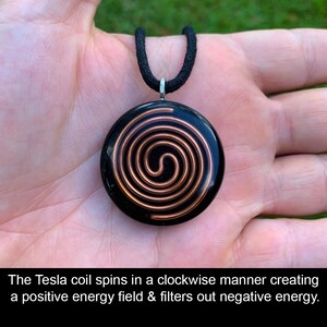 May include: Black pendant with a copper spiral design, suspended from a black cord. The pendant's text reads: "The Tesla coil spins in a clockwise manner creating a positive energy field & filters out negative energy."