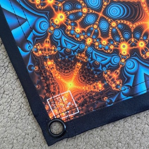 May include: A tapestry with a psychedelic fractal pattern in shades of blue, orange, and yellow. The tapestry has a black border with a white "PUMA" logo and a metal grommet.