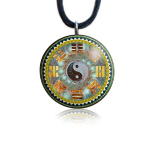 May include: Round pendant with a Yin Yang symbol at the center, surrounded by a detailed design in shades of blue, gold, and brown. The pendant is suspended from a black cord. The design includes geometric shapes and a scalloped edge.