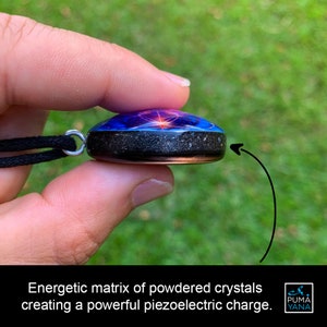 May include: A round pendant with a black cord. The pendant has a blue and purple design on top, a black center, and a copper-colored edge. The text on the image reads: "Energetic matrix of powdered crystals creating a powerful piezoelectric charge."