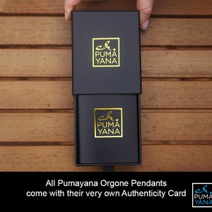 May include: Black box with a gold logo that reads "Puma Yana". The box is open, revealing a smaller box with the same logo. The text at the bottom reads "All Pumayana Orgone Pendants come with their very own Authenticity Card."