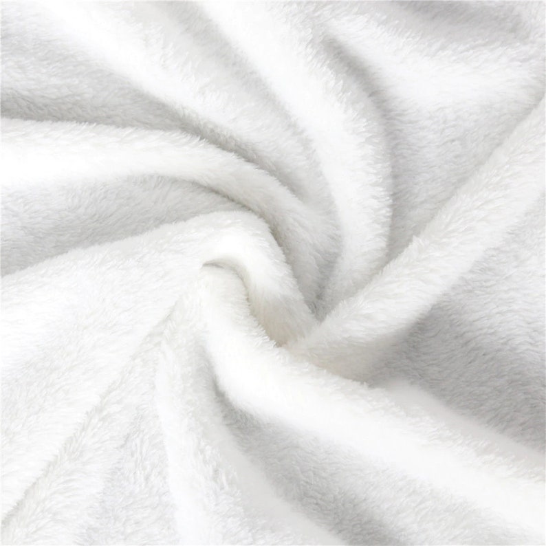May include: Close-up of a soft, white, plush blanket. The fabric is thick and fluffy, with a deep pile that creates shadows and highlights. The blanket is folded and swirled, showing the texture and depth of the material.