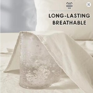 May include: A clear, textured glass tumbler is partially covered by a piece of off-white fabric. Above the fabric, the text "LONG-LASTING BREATHABLE" is displayed in dark brown letters, accompanied by a small icon of three horizontal lines.