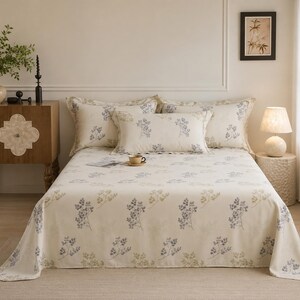 May include: A bed set featuring a cream-coloured bedspread and matching pillowcases decorated with a repeating pattern of small, delicate blue and green floral sprigs. The set includes two standard pillows and one rectangular accent pillow.