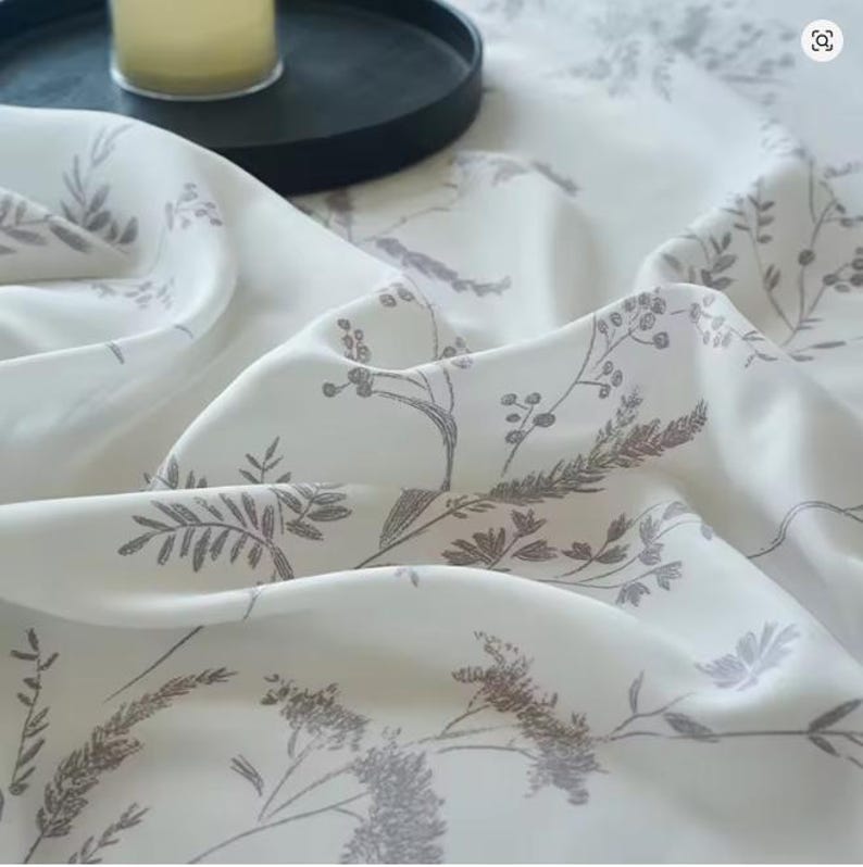 May include: A white fabric featuring a delicate, repeating botanical print in a soft grey tone. The pattern consists of fine-lined illustrations of various wild grasses, stems, and small clusters of berries scattered across the smooth surface.