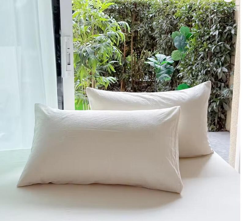 May include: Two rectangular pillows with a solid off-white, textured fabric cover. The pillows are arranged with one positioned slightly in front of the other, featuring clean, straight edges and a simple, uniform appearance across the surface.