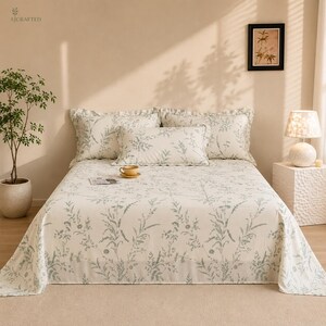 May include: A bed set featuring a cream-coloured bedspread and two matching pillow shams, all decorated with a repeating light green botanical print of wildflowers and grasses. The bedding is arranged on a bed with a central rectangular pillow.
