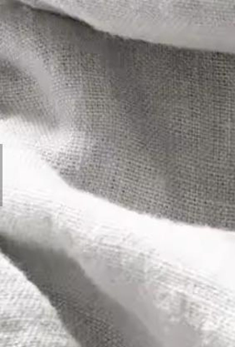 Op de afbeelding: Een textielstof met een herhalend patroon van brede horizontale strepen in afwisselende tinten wit en lichtgrijs. Het materiaal vertoont een zichtbare geweven textuur met een consistent rasterachtig weefpatroon over het gehele oppervlak.