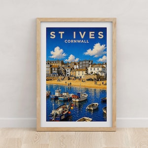 May include: A framed art print featuring a coastal scene of St. Ives, Cornwall. The image displays a sandy beach with buildings, blue water, and several small fishing boats. The text ST IVES CORNWALL is printed in white at the top of the print.
