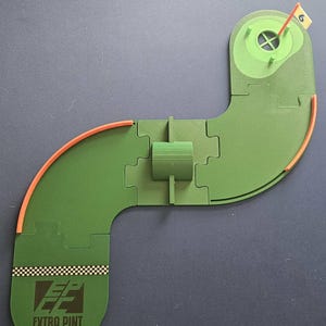 May include: Green Crokinole board puzzle with orange borders and a flag at the end. The board is shaped like a golf course. The text "EXTRA PINT CROKINOLE CLUB" is printed on the board.