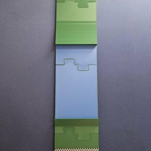 May include: A green and blue puzzle-like game piece with a golf course design. The top section features a golf hole with a flag, labeled with the number 1. The bottom section has the text "EXTRA PINT CROKINOLE CLUB".