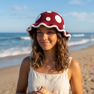 May include: A burgundy crochet hat with white polka dots and a white scalloped brim. The hat is a mushroom-style design, perfect for sun protection. The hat is worn outdoors on a sunny day.