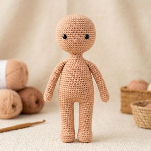 May include: A crocheted doll in a light brown color, with a rounded head, small black eyes, and a simple body. The doll has arms and legs, and is made with a tight stitch pattern. The doll is a blank canvas for customization.