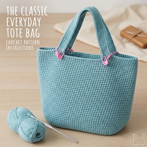 Pode incluir: Uma sacola tote de crochê azul claro com uma bola de lã e uma agulha de crochê correspondentes. A sacola tem formato retangular com duas alças e marcadores de ponto rosa. O texto na imagem diz "THE CLASSIC EVERYDAY TOTE BAG CROCHET PATTERN INSTRUCTIONS."