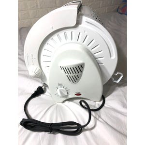 May include: A white circular electric food dehydrator with a black power cord and plug. The front panel features a timer dial labelled in minutes from off to 120, a red power indicator light, and a small knob on the side marked with an open arrow.
