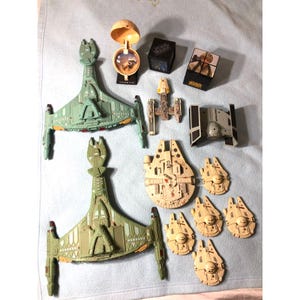 Peut inclure: Une collection de jouets Star Wars comprenant deux vaisseaux spatiaux verts, un chasseur TIE, un Y-wing, un grand et quatre petits vaisseaux Faucon Millenium, un globe Tatooine et deux cubes noirs avec la marque Star Wars et des images de personnages.