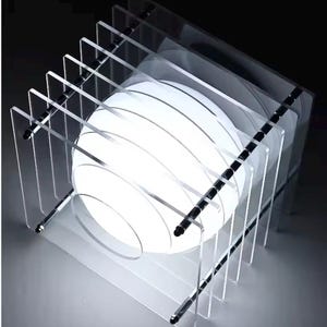 May include: A table lamp featuring a series of parallel, clear acrylic square panels held together by four metal rods. A bright, spherical white light source is positioned in the center, creating a glowing effect through the transparent layers.