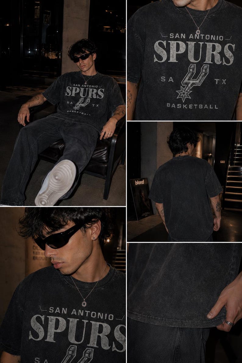 May include: A charcoal gray short-sleeve t-shirt featuring a distressed graphic print that reads SAN ANTONIO SPURS with the team logo, SA, and TX. The shirt has a crew neckline and a washed-out, vintage-inspired texture throughout the fabric.