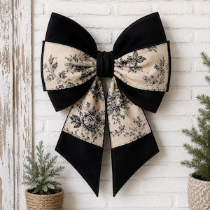 May include: A large decorative bow with a black velvet exterior and a cream-colored floral patterned center. The bow is mounted on a white brick wall, and is a decorative accent for home decor.