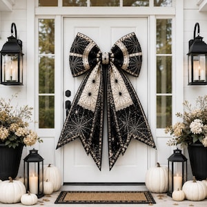 May include: A large black and cream bow with a spiderweb pattern adorns a white door. The Halloween-themed porch features pumpkins, lanterns, and potted plants, creating a festive atmosphere.