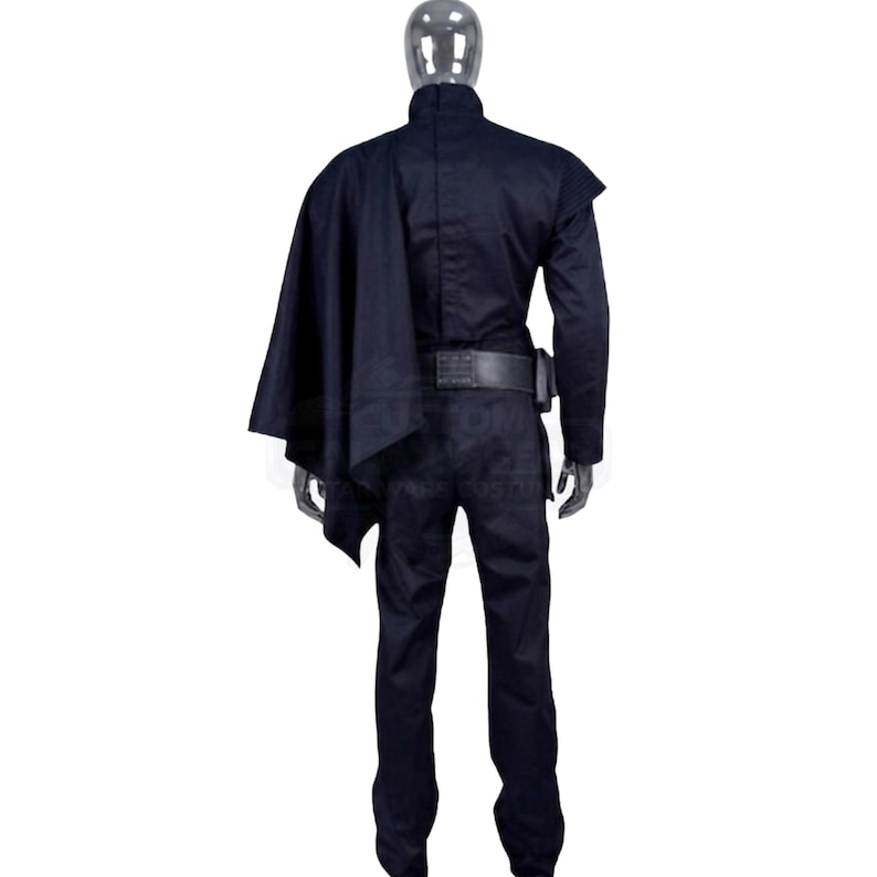 May include: A dark navy blue long-sleeved jumpsuit worn by a mannequin, featuring a high collar, a structured shoulder panel, a matching dark cape draped over the right shoulder, and a wide black utility belt secured around the waist area.
