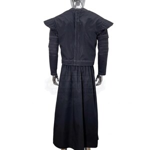 K&ouml;nnte beinhalten: Ein schwarzes Ensemble aus einer lang&auml;rmeligen Jacke und einem bodenlangen Rock auf einer Schaufensterpuppe. Die Jacke hat strukturierte Schulterpolster, horizontale Steppn&auml;hte an den &Auml;rmeln und eine vertikale Naht in der Mitte des R&uuml;ckens.
