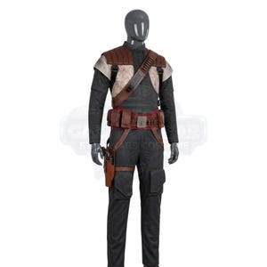 May include: A dark gray mannequin wearing a costume consisting of a black long-sleeved shirt and matching trousers with cargo pockets. It features a brown leather-like chest harness, a utility belt with pouches, and a holster with a sidearm.