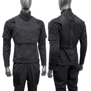 May include: Black tactical uniform displayed on a mannequin. The outfit includes a high-collared shirt, a chest plate, and matching pants. The sleeves have geometric patterns, and the uniform appears to be made of a durable, matte material.